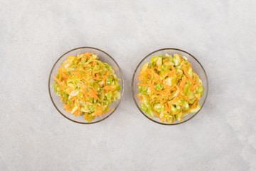 Vegetable salad with cabbage and carrots in a bowl on a light background top view