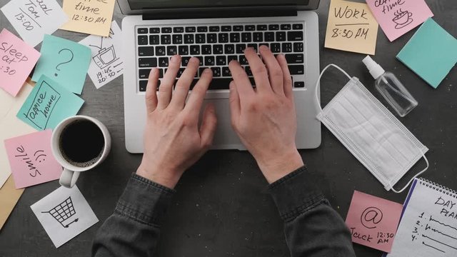 Male hands typing on laptop keyboard, top view. Freelancer working on desktop computer. Office table workspace.