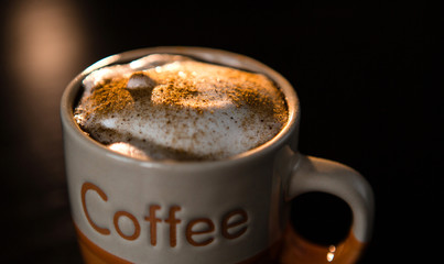 Close up of delicious cappuccino with cinnamon and milk foam in cup on dark table.