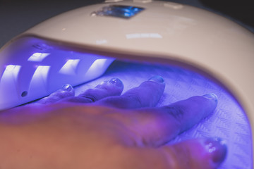 Woman includes lamp and dries her nails with shellac in UV lamp. Close-up.