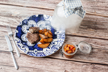 Grilled steak with baked golden potatoes on a wooden background. Top view. Delicious Recipe. Pork Fillet Cooked on Skillet for Dinner . Fried Juicy Meat Texture. Horizontal photo.