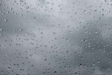 Raindrops on a car window against grey overcast sky