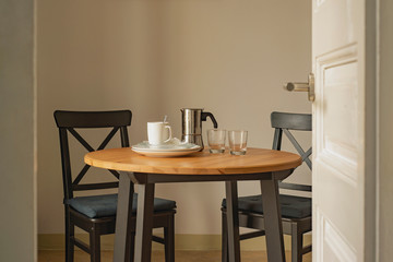 After breakfast home interior set with wooden table, black chairs, coffee maker, glasses, and empty dishes