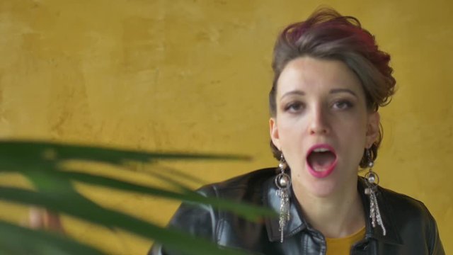 Let's rock concept. Portrait of excited aggressive beautiful woman with dark pink hair in casual yellow dress standing, looking at camera, showing rock and roll gesture.