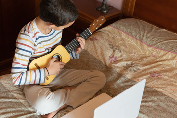 Side view of a little boy playing timple at home.