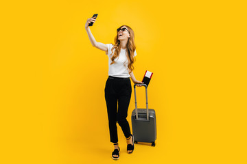 woman in sunglasses taking a selfie on a mobile phone, standing with a suitcase and a passport with...