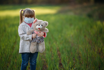 Masked girl holding a bear in the park. Copy space