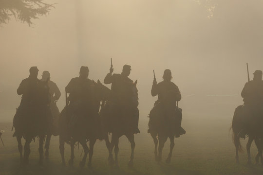 Group of silhouetted Soldiers on Horseback with Guns in the air moving forward in the smokey haze toward the battle in the American Civil War
