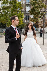 Naklejka premium Bride and groom dancing in the old town street. Wedding couple walks in Budapest near Parliament House. Caucasian happy romantic young couple celebrating their marriage. Wedding and love concept.