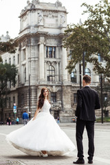 Bride and groom dancing in the old town street. Wedding couple walks in Budapest near Parliament House. Caucasian happy romantic young couple celebrating their marriage. Wedding and love concept.
