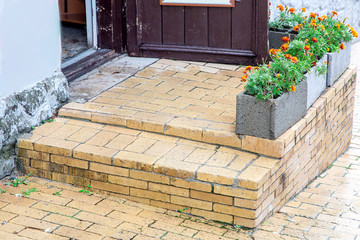 brick threshold with a step at the open wooden entrance door with gray stone flowerpots for flowers, a closeup of architectural details.