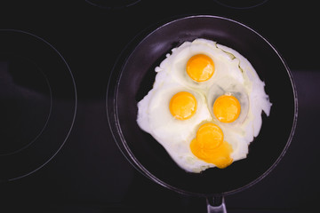 Fried eggs in frying pan. Four eggs. Making breakfast for family. Family weekend breakfast. Quick easy brunch breakfast. Over medium fried eggs. Egg yolk, egg whites. Black stove top. Broken egg yolk