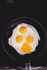 Fried eggs in frying pan. Four eggs. Making breakfast for family. Family weekend breakfast. Quick easy brunch breakfast. Over medium fried eggs. Egg yolk, egg whites. Black stove top. Broken egg yolk
