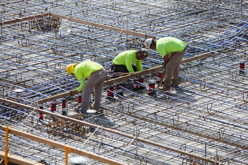 Three concrete construction workers tying rebar and setting concrete forms for building construction - obrazy, fototapety, plakaty