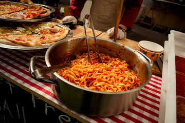 Italian pasta in a large saucepan with tomato sauce. Slices of pizza on a tray.