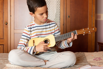 Front view of a little boy playing timple at home.