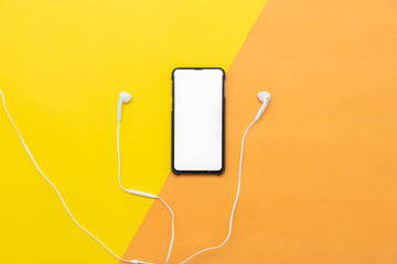 Obraz premium White headphones with the phone isolated on yellow/orange background.