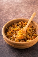 Organic dried golden raisins in wooden bowl.Brown background, vertical format