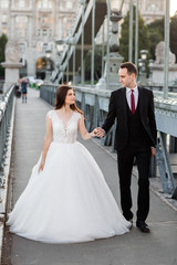 Naklejka premium Bride and groom hugging in the old town street. Wedding couple walking on Szechenyi Chain Bridge, Hungary. Happy romantic young couple celebrating their marriage. Wedding and love concept.