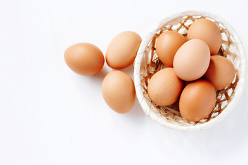 Brown chicken eggs in a straw basket on white wooden background. Top view with copy space.