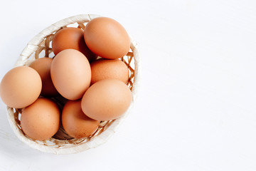 Brown chicken eggs in a straw basket on white wooden background. Top view with copy space.