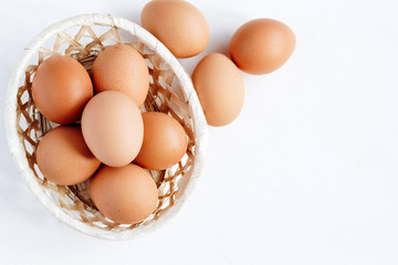 Brown chicken eggs in a straw basket on white wooden background. Top view with copy space.