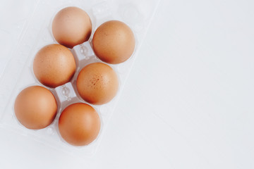 Brown chicken eggs in plastic container on white wooden background. Top view with copy space.