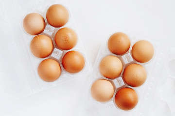 Brown chicken eggs in plastic container on white wooden background. Top view.
