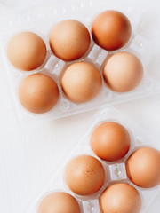 Brown chicken eggs in plastic container on white wooden background. Top view.