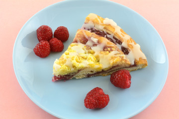 Slice of raspberry breakfast danish and fresh raw raspberries on blue breakfast plate on pink background