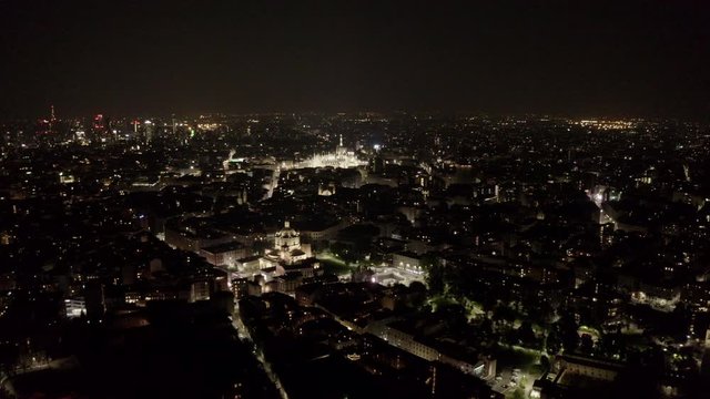 Aerial view of Milan, Italy city center with Duomo cathedral and Porta Nuova skyscrapers seen from drone flying in the sky at night. Italian urban landscape in Milano with buildings and streets