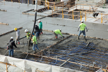 Concrete construction crew leveling cement floor of multi-story building at building site. Workings...