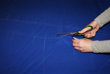 The female hand cuts the fabric with scissors, cutting the fabric.