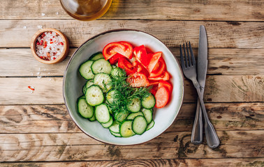 Healthy vegetable salad of fresh tomato, cucumber, dill and spices and oil in bowl on rustic wooden background. Diet concept.
