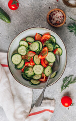 Healthy vegetable salad of fresh tomato, cucumber, dill and spices and oil in bowl on light gray background. Diet concept.