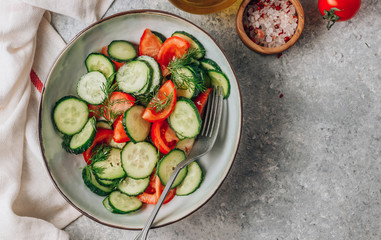 Healthy vegetable salad of fresh tomato, cucumber, dill and spices and oil in bowl on light gray background. Diet concept.