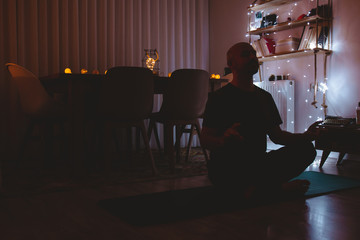Young man doing yoga for peace in the dark in his house