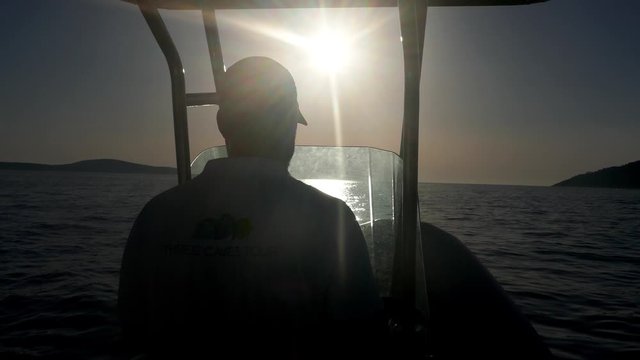 Rear shot behind a silhouette speed motorboat helmsman skipper navigating fast in sea with sun in background