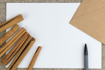 Cinnamon sticks, mechanical pencil, envelope, lie on a white sheet of paper, on a rough linen cloth