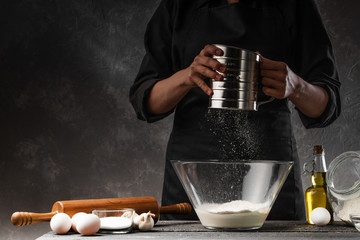 Chef cooks dough. With flour frozen in motion. Against the background of ingredients. Cooking flour products, bread, Italian pasta, rolls and pastries. With space for inscription bakery display cases © Anton