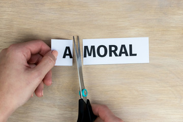Woman cuts by scissors word "amoral", written on paper, so that word "moral" is obtained.