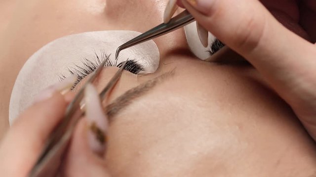 Eyelashes extensions. Fake eyelashes. Eyelash extension procedure.Close up portrait of woman eye with long eyelashes. Professional stylist lengthening female lashes. Master and client in beauty salon.