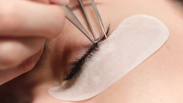 Eyelashes extensions. Fake eyelashes. Eyelash extension procedure.Close up portrait of woman eye with long eyelashes. Professional stylist lengthening female lashes. Master and client in beauty salon.
