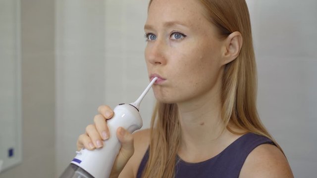 A young woman uses a portable water flosser dental oral Irrigator to clean her teeth. Teeth care concept