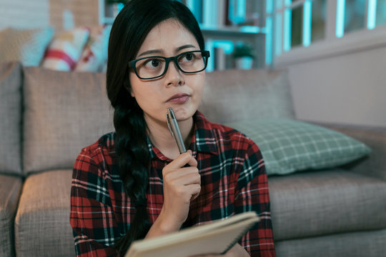 female student looking aside is thinking about her study plan for next week. portrait of a young woman holding pen and notebook with a thoughtful look.