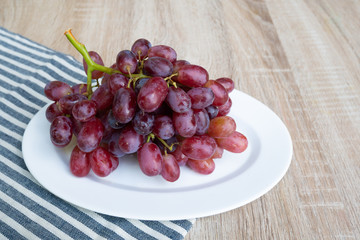 There​ are​ grapes fruits​ in​ a​ white​ dish on​ the​ wooden​ table.