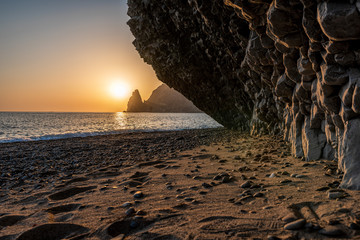 view of the sunset sea and the beach, the volcanic rock is lit by the warm sunset, sand and pebbles, volcanic basalt as in Iceland. Copy space. The concept of calmness, silence and unity with nature.