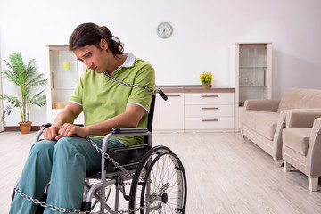Young male invalid in wheel-chair suffering at home