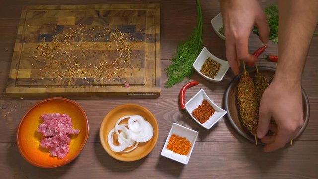 Lulia kebab, a dish of Georgian cuisine. Process of making kebab lula, top view. Chef cooks a lula kebab from raw minced meat and sprinkled with spices. Spices and ingredients stand on the table.
