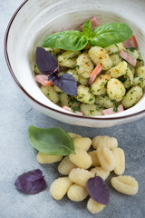 Close-up of potato gnocchi served with basil pesto sauce and chopped bacon in a bowl, vertical shot
